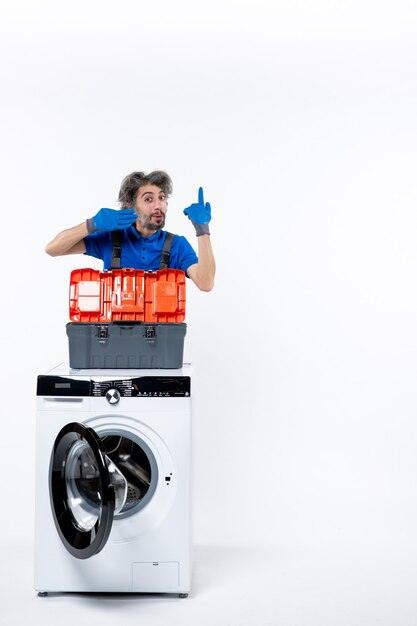 Front view male repairman showing his drain gloves behind washing machine on white space