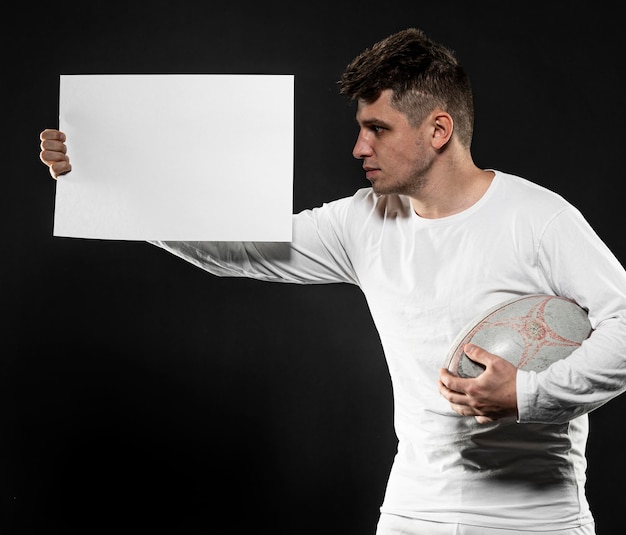 Front view of male rugby player holding ball and blank placard