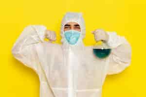 Free photo front view male scientific worker in special protective suit holding flask with blue solution flexing on yellow surface