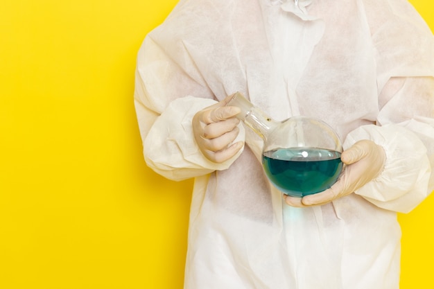 Front view of male scientific worker in special protective suit holding flask with green solution on yellow wall