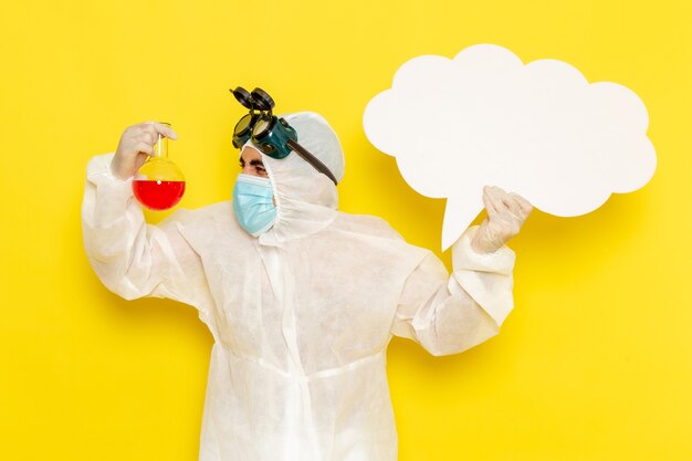 Front view male scientific worker in special protective suit holding flask with red solution big white sign on yellow surface