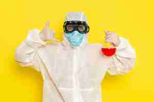 Free photo front view male scientific worker in special protective suit holding flask with red solution and posing on the yellow surface