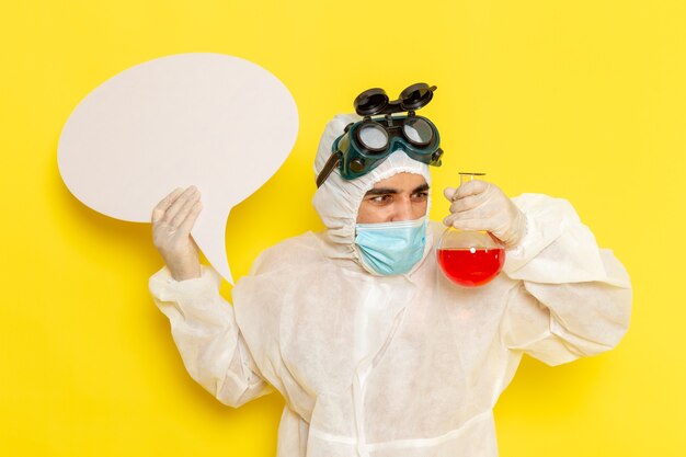 Free photo front view male scientific worker in special protective suit holding flask with red solution and white sign on yellow surface