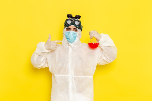 Front view male scientific worker in special protective suit holding flask with red solution on the yellow surface