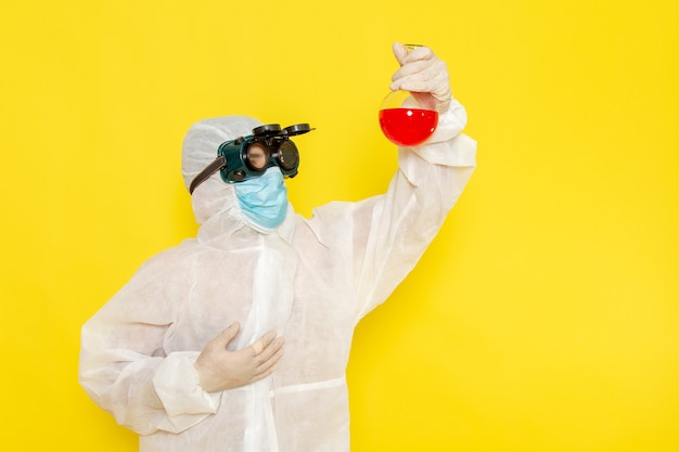 Front view male scientific worker in special protective suit holding flask with red solution on yellow surface