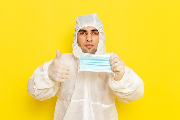 Front view of male scientific worker in special protective suit holding his mask on the yellow wall