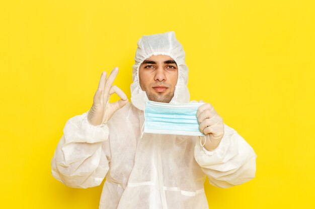 Front view of male scientific worker in special protective suit holding his mask on yellow wall