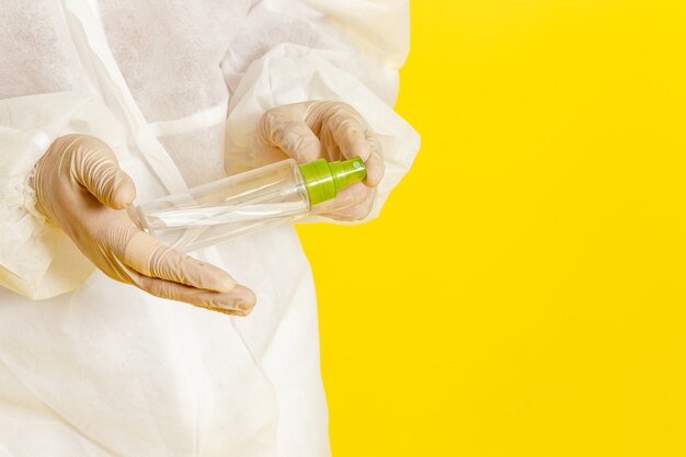 Front view male scientific worker in special protective suit holding spray flask on the light yellow surface