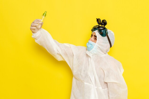 Front view male scientific worker in special protective suit holding spray flask on yellow desk