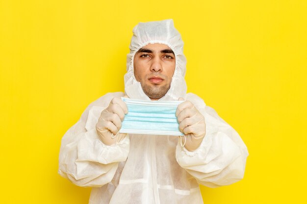 Front view of male scientific worker in special protective suit taking off his mask on light-yellow wall