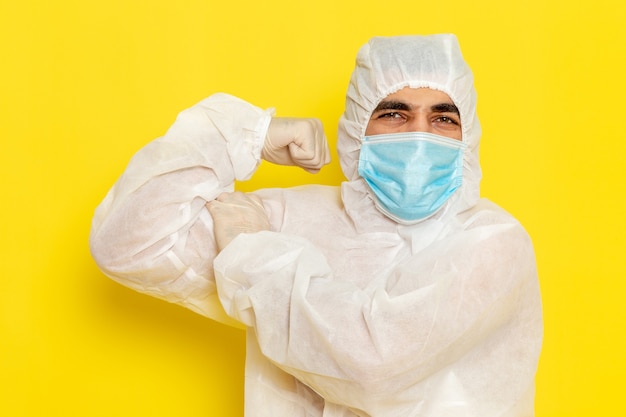 Foto gratuita vista frontale del lavoratore scientifico maschio in tuta protettiva speciale e con maschera che flette sul muro giallo chiaro