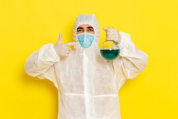 Front view of male scientific worker in special protective suit with mask holding flask on yellow desk science worker costume color danger photo