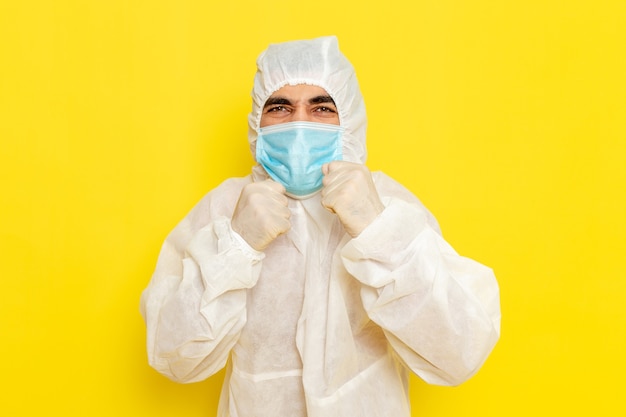 Вид спереди научного работника-мужчины в специальном защитном костюме и с маской на светло-желтой стене