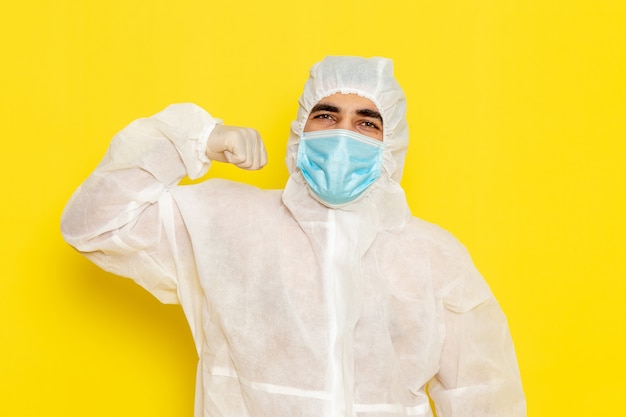 Free photo front view of male scientific worker in special protective white suit with mask flexing on light-yellow desk science worker scientific chemistry color danger