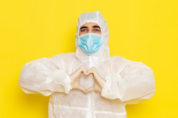 Foto gratuita vista frontale del lavoratore scientifico maschio in vestito bianco protettivo speciale con la maschera sul pericolo di colore di chimica scientifica del lavoratore di scienza della scrivania giallo chiaro