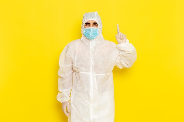 Front view of male scientific worker in special protective white suit and with mask posing on yellow wall