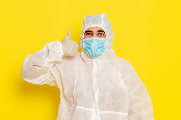 黄色の机の上のマスクと特別な保護白いスーツを着た男性の科学者の正面図科学者科学化学色の危険
