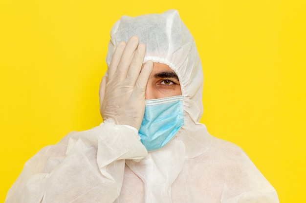 黄色の壁に彼の顔の半分を覆う滅菌マスクと特別な保護白いスーツを着た男性の科学者の正面図