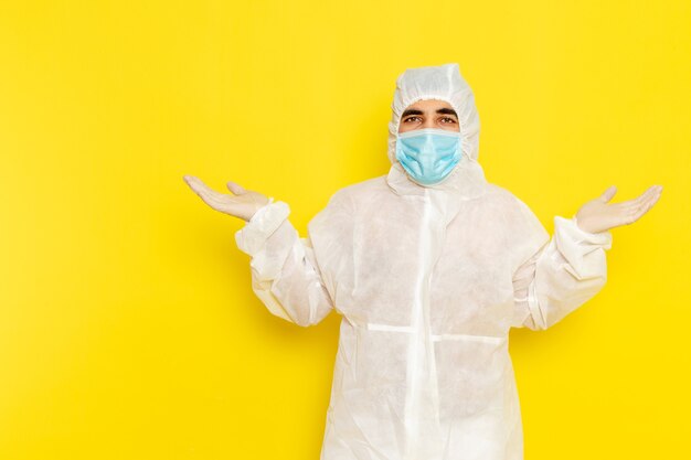 Front view of male scientific worker in special protective white suit with sterile mask on yellow wall