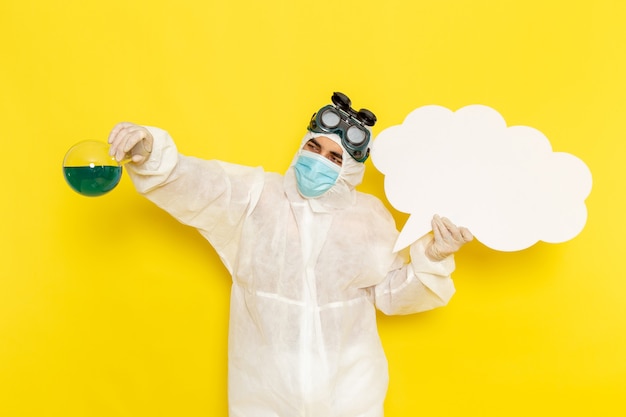 Free photo front view male scientific worker in special suit holding flask with green solution and huge white sign on the yellow desk