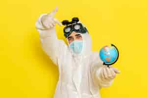 Free photo front view male scientific worker in special suit holding little round globe posing on yellow desk