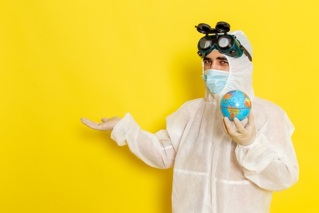 Free photo front view male scientific worker in special suit holding little round globe on the yellow desk