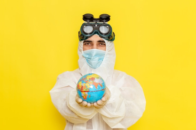 Вид спереди мужской научный работник в специальном костюме, держащий маленький круглый глобус на желтом полу
