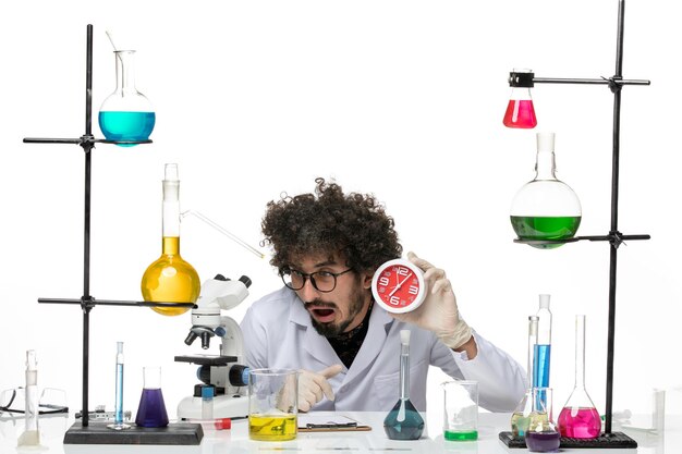 Front view male scientist in medical suit holding red clocks on light-white space