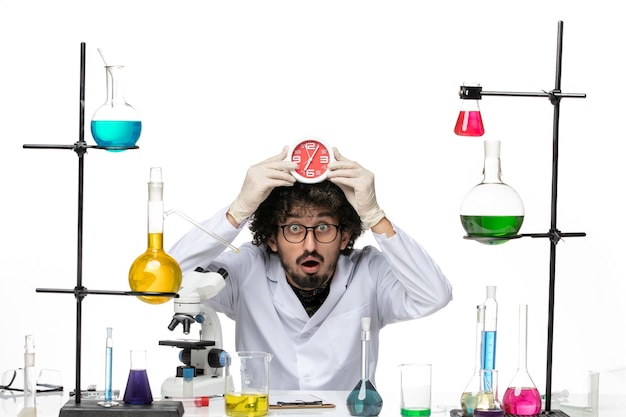 Front view male scientist in medical suit holding red clocks on light-white space