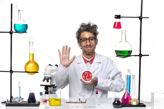 Front view male scientist in medical suit holding round clocks and smiling on white background chemistry covid- lab virus health