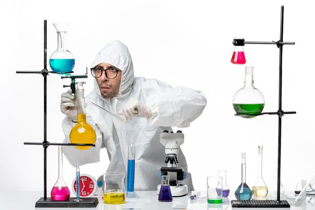 Front view male scientist in special protective suit around table with solutions