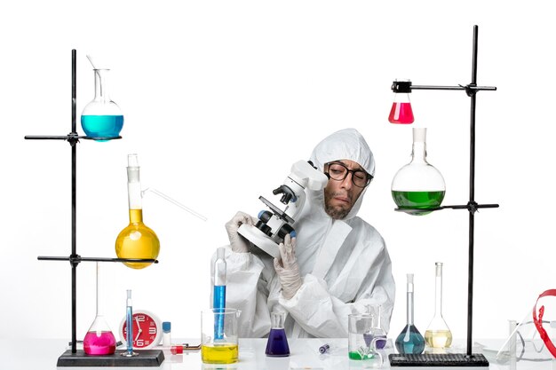 Front view male scientist in special protective suit holding microscope