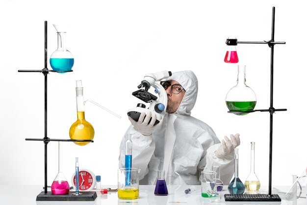 Front view male scientist in special protective suit holding microscope