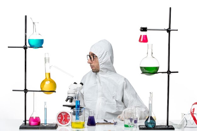 Front view male scientist in special protective suit sitting around desk with solutions