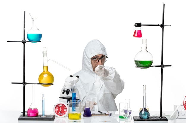 Front view male scientist in special protective suit sitting around desk with solutions