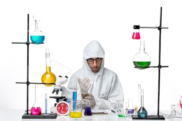 Front view male scientist in special protective suit sitting around table with solutions