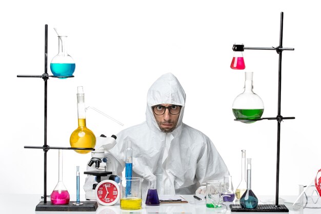 Front view male scientist in special protective suit sitting around table with solutions