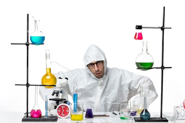 Front view male scientist in special protective suit sitting with different solutions