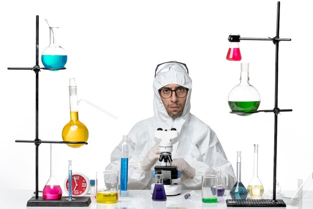 Вид спереди ученый-мужчина в специальном защитном костюме с помощью микроскопа