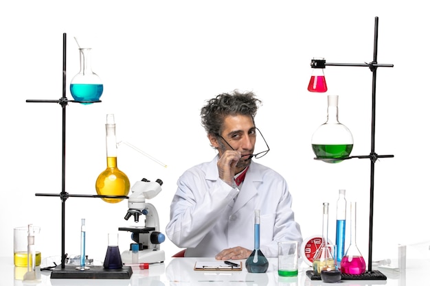 솔루션 테이블 앞에 앉아 흰색 의료 소송에서 전면보기 남성 과학자