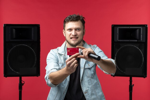 Front view of male singer performing on stage holding bank card on a red wall