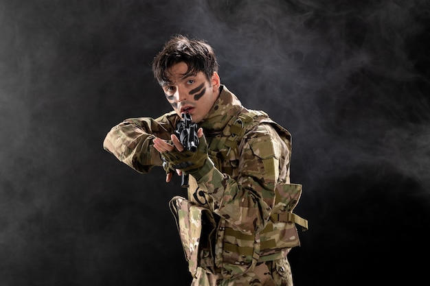 Вид спереди мужчины-солдата в камуфляжной винтовке на темной стене