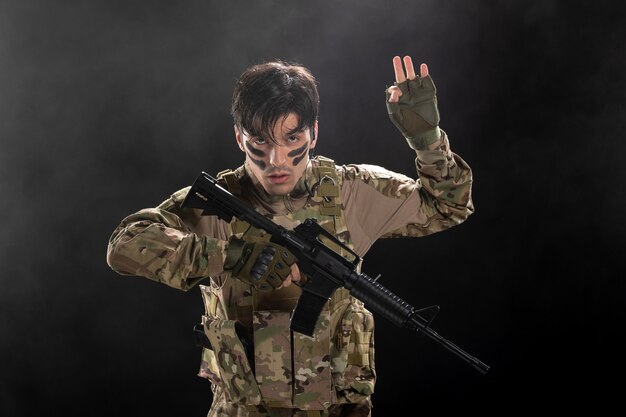 Front view of male soldier fighting during operation with rifle on dark wall