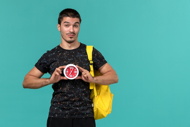 Free photo front view of male student in dark t-shirt yellow backpack holding clocks on light blue wall