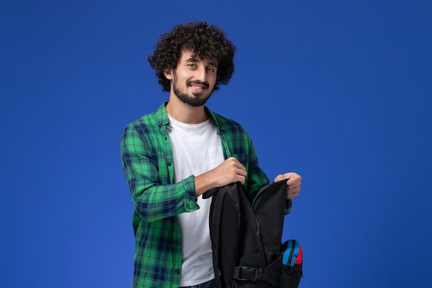 밝은 파란색 벽에 검은 가방을 들고 녹색 체크 무늬 셔츠에 남성 학생의 전면보기