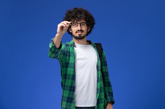 Front view of male student in green checkered shirt smiling on blue wall