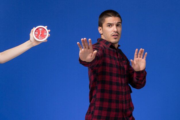 Free photo front view of male student in red checkered shirt with backpack posing on blue wall