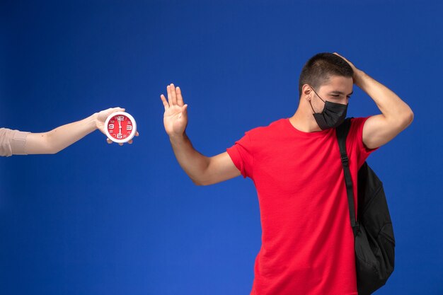 青い背景にポーズをとってマスクとバックパックを身に着けている赤いTシャツの正面図男子学生。