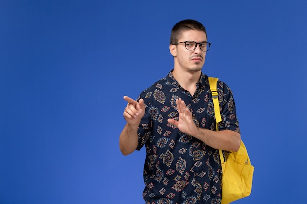 青い壁に不快な表情でポーズをとって黄色のバックパックを身に着けている男子学生の正面図