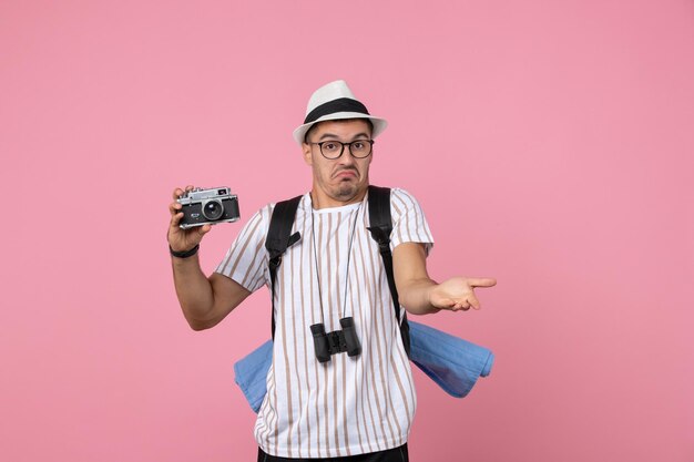 Front view male tourist holding camera for photos on pink wall emotion tourist color